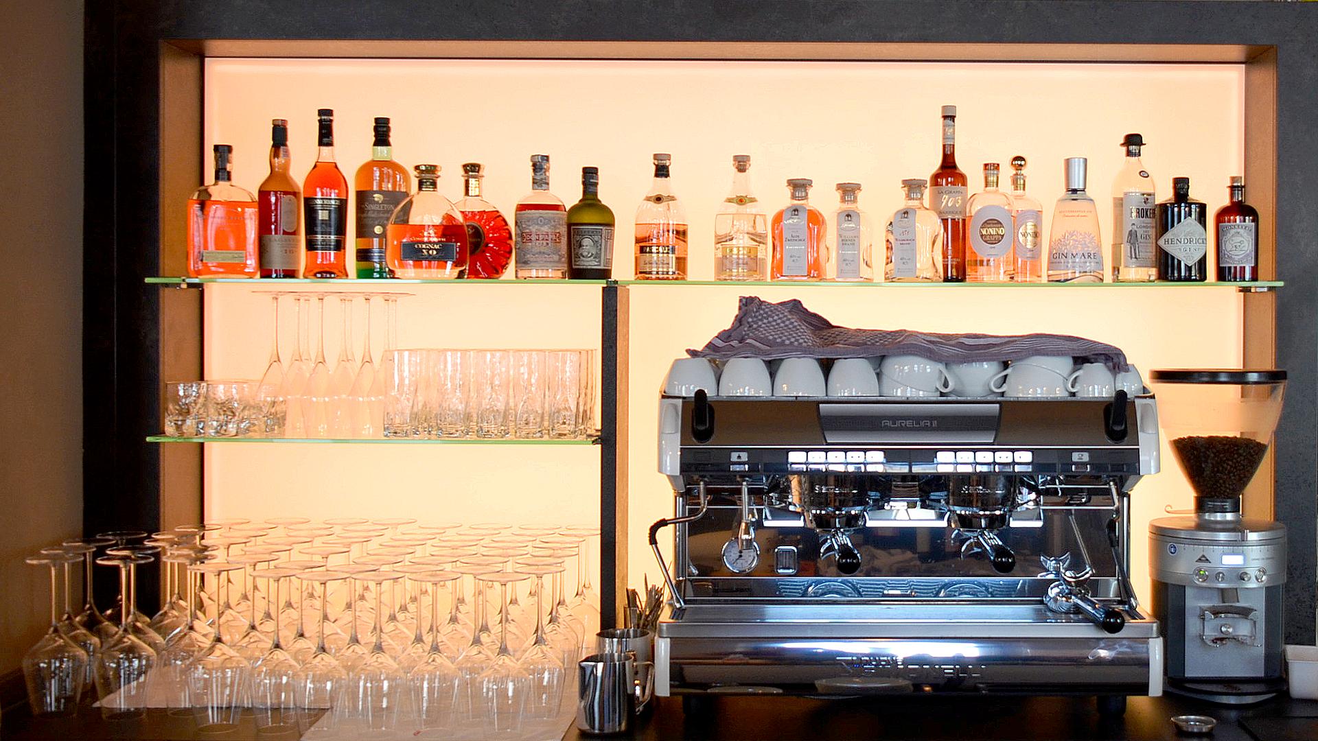 Bild: Café & Weinbar achtzehn97 im EG nach der Sanierung - Tresen mit Espressomaschine und beleuchtetem Spirituosenregal